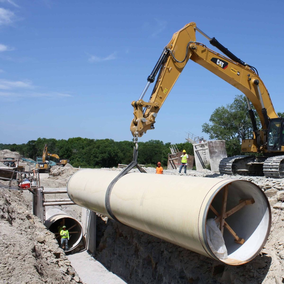 Excavator lowering a large water pipe into a trench